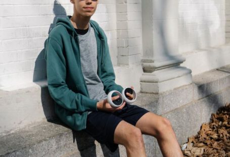 Virtual Fitness - Full body of young male in sportswear and VR goggles sitting on concrete foundation of white building and holding controllers
