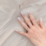 Fine Jewelry - Hands of a Person Wearing Silver Ring on White Sand