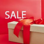 Luxury Deals - Cardboard Box with Red Ribbon Beside A Sale Sign